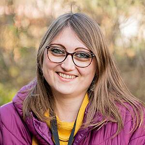 Woman smiling outdoors wearing glasses.