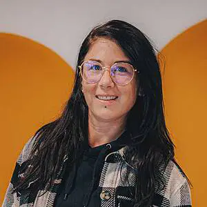 Woman smiling with glasses, orange background.