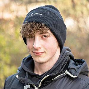Young man with beanie smiling outdoors.