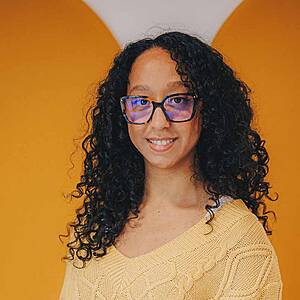 Woman with glasses, yellow sweater, smiling.