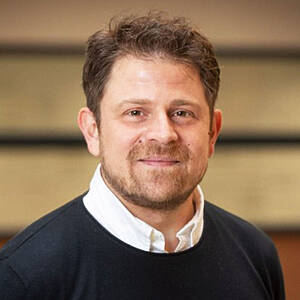 Smiling man in black sweater and shirt.