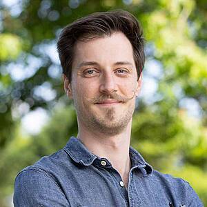 Man with mustache smiling outdoors.
