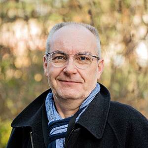 Man smiling outdoors with glasses.