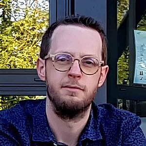 Man with glasses, blue shirt, outdoor setting.