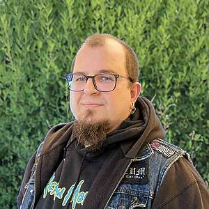 Man smiling outdoors wearing glasses and earring.