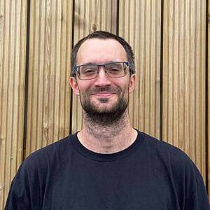 Man smiling with glasses, wooden background.
