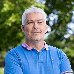 Man smiling outdoors in blue polo shirt.