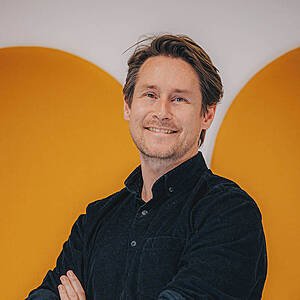 Smiling man with crossed arms, yellow background.