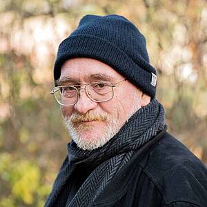 Elderly man wearing glasses and beanie outdoors.