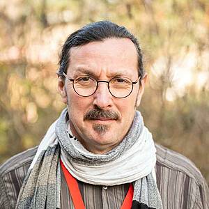 Man with glasses and scarf outdoors.