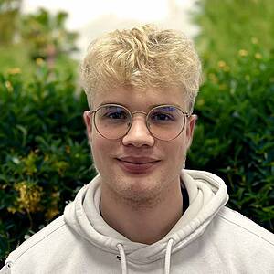 Young man with glasses, smiling, outdoors.