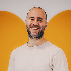 Smiling man with beard against yellow background.