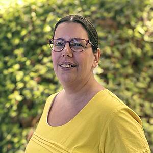 Woman in yellow top, glasses, smiling.