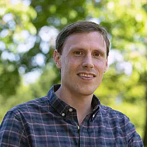 Man smiling outdoors in plaid shirt.